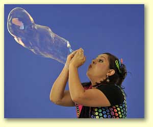 Bernadette blowing a big, long bubble from her bare hands.